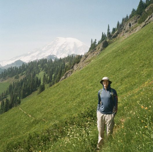 Man standing in mountain meadow, with Mt Rainier in the background