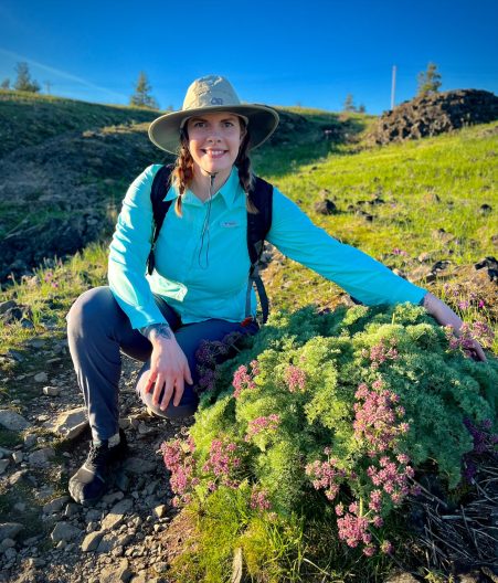 Woman sitting on a mountain hillside next to a large flowering plant