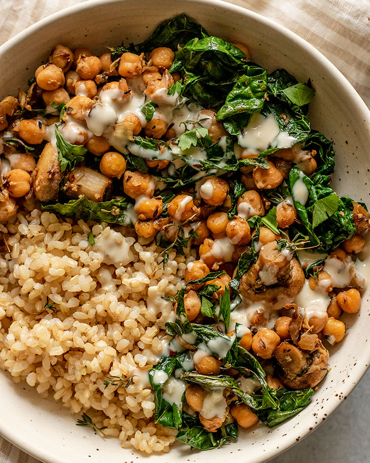 Large bowl of rice served with sautéed chickpeas and kale topped with creamy dressing.